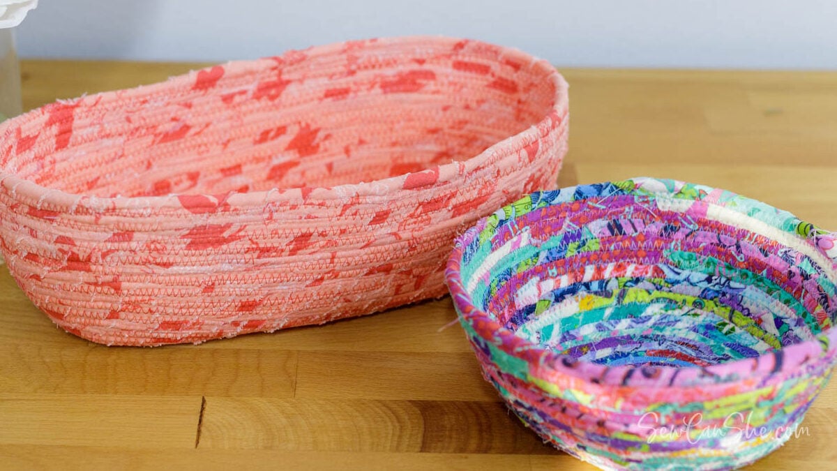 Two colorful handmade rope bowls made from fabric scraps, displayed on a wooden surface for a craft fair.
