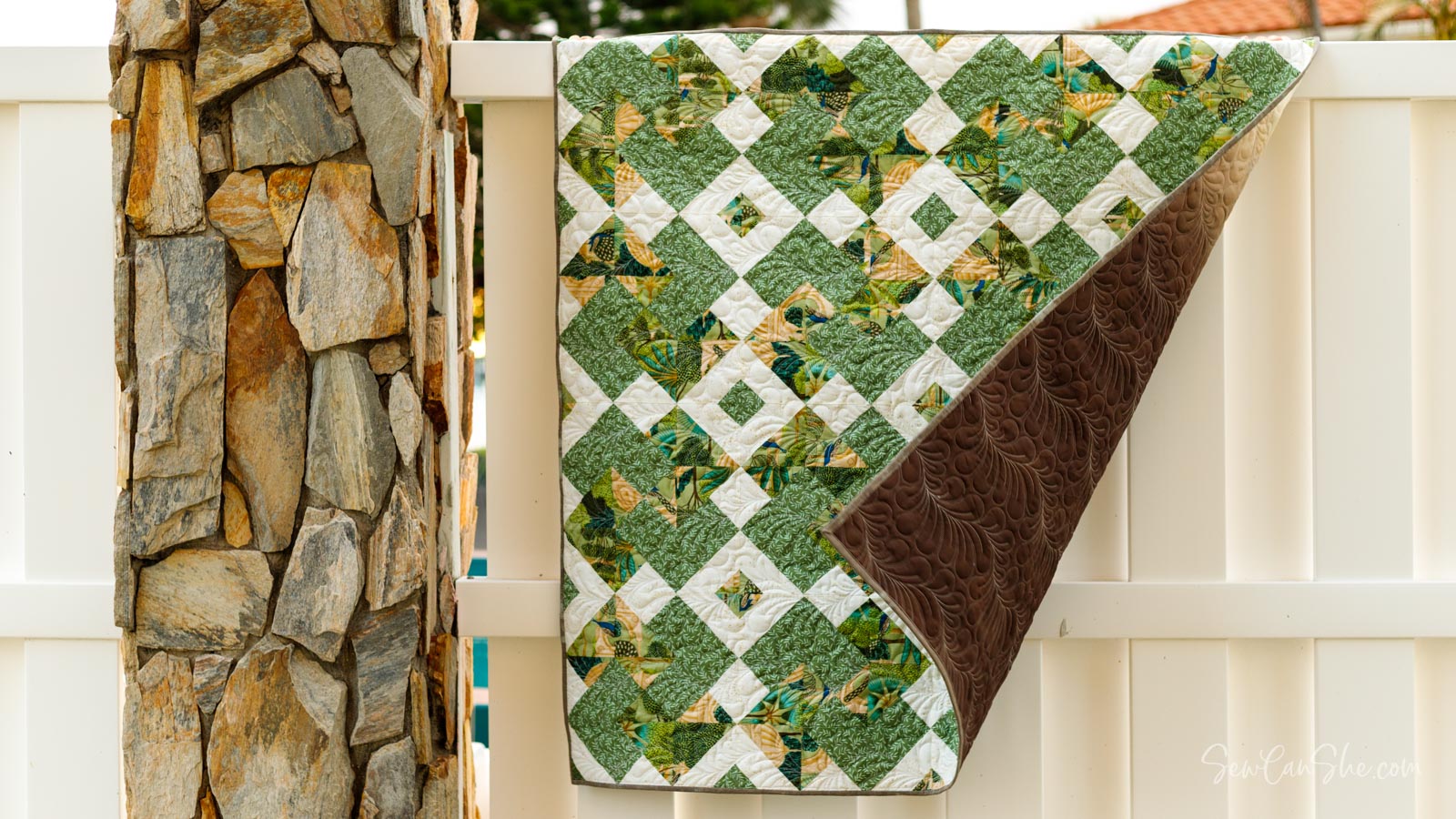 Green and white quilt hanging on fence
