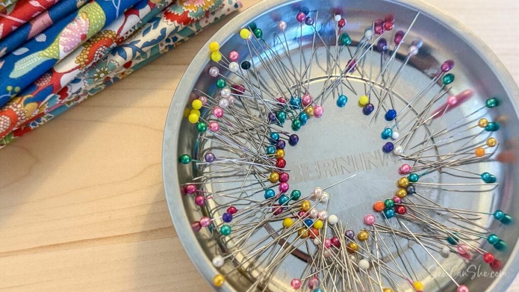 A magnetic pin bowl filled with colorful head sewing pins on a sewing table.