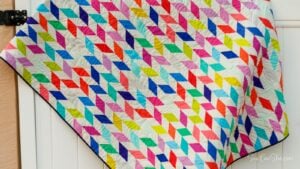 Colorful jelly roll strip quilt hanging on door. It is sewn with lots of bright solid fabric.