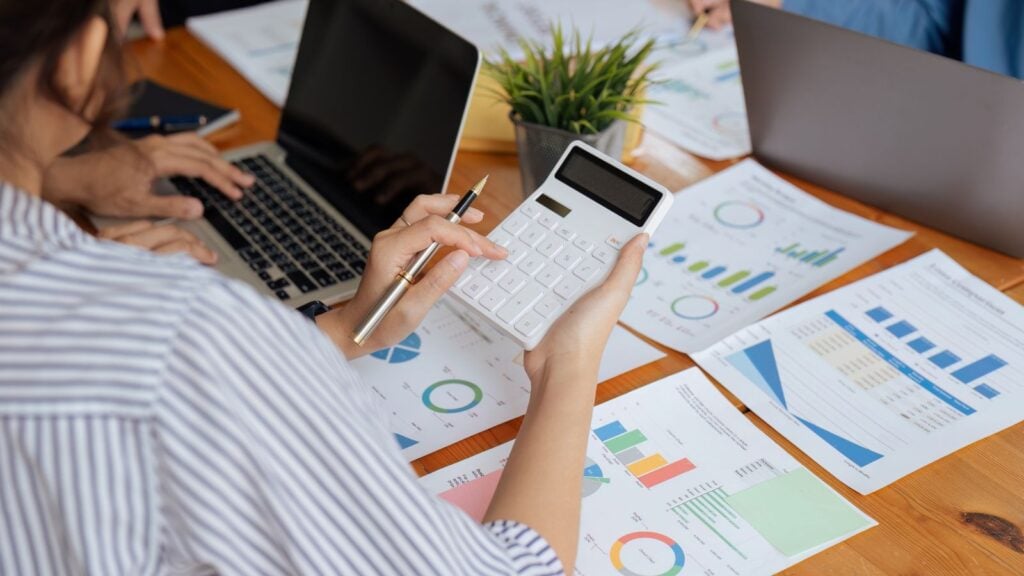 Businesswoman using a calculator to calculate numbers on a company's financial documents, she is analyzing historical financial data to plan how to grow the company. Financial concept.