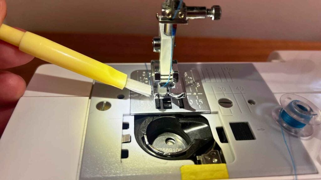 Brushing lint and dust from the feed dogs and bobbin case as routine sewing machine maintenance.