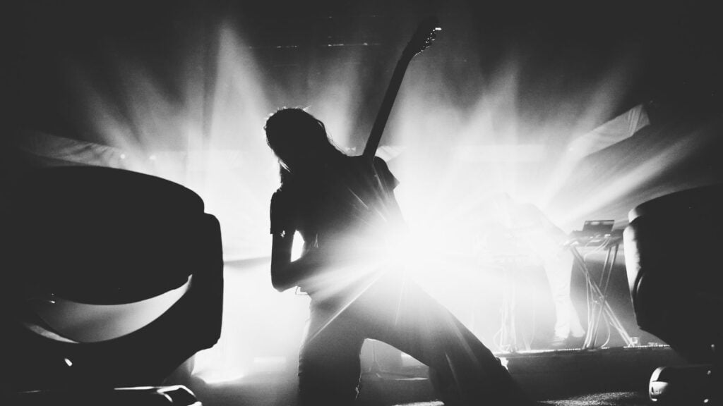Female guitarist silhouette playing guitar solo on a stage on a knees