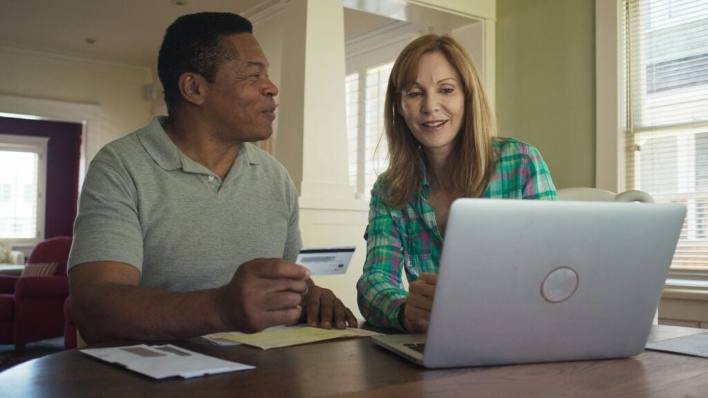 Happy older couple booking trip or making purchase online with credit card using laptop computer