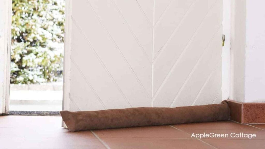 Brown suede dust and pollen blocker and draft stopper in front of a clean white door. A perfect sewing pattern for Spring cleaning.