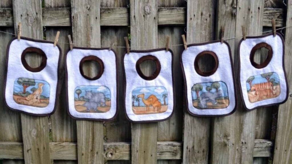 five handmade baby bibs hanging on a fence to display baby sewing patterns