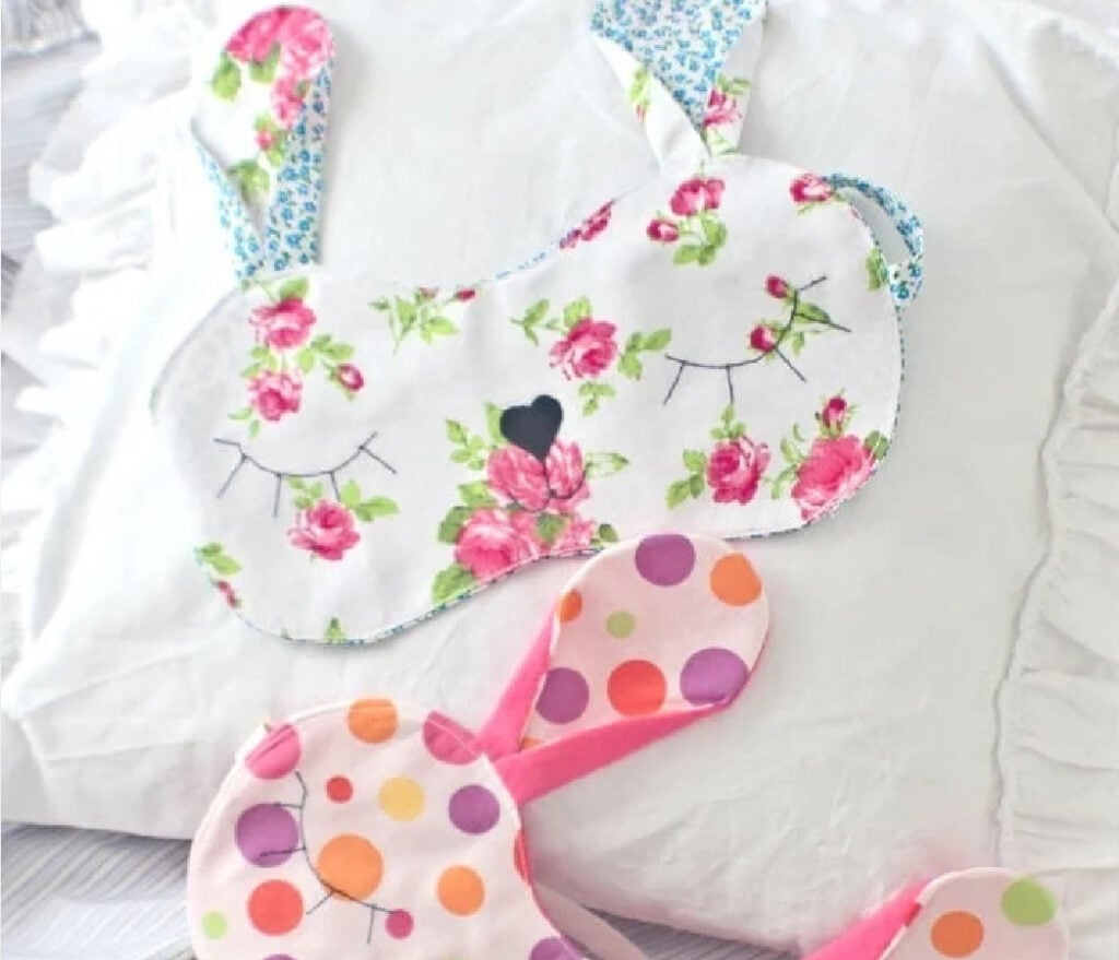 A handmade fabric sleeping mask shaped like a bunny face with soft pink ears, a quick 30-minute sewing gift.