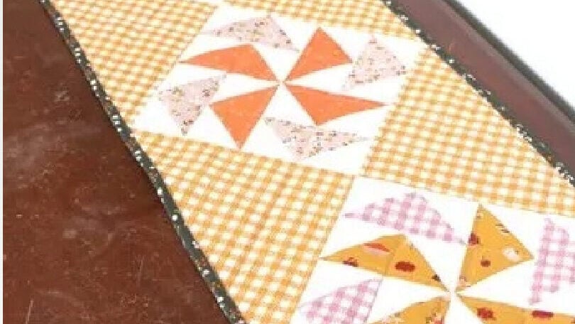 Traditional Dutchman's Puzzle quilt blocks featuring orange and white windmill patterns arranged into a long table runner.