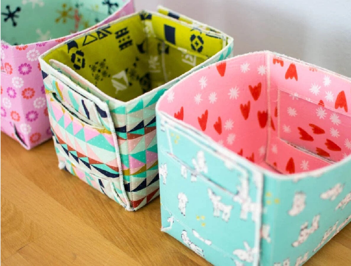 Handmade fold-up fabric baskets; one features a colorful geometric triangle print and the other a light blue fabric with heart and bunny patterns, both shown with their sides snapped together.