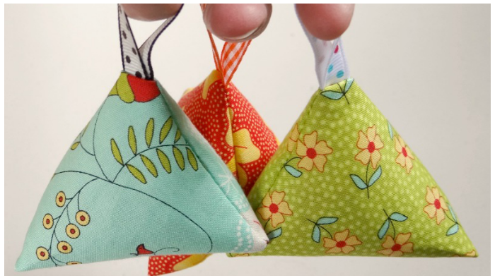 Lavender Sachets: Three pyramid-shaped fabric sachets made from colorful scrap fabric, tied with twine and decorated with small sprigs of lavender.