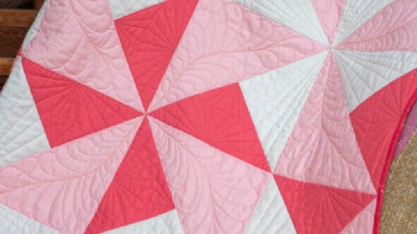 A soft handmade baby quilt featuring pink, blue, and yellow geometric pinwheel patterns on a white background.
