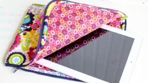 Brightly quilted iPad sleeve in a modern floral print showing a white iPad peeking out of its protective padded pocket.