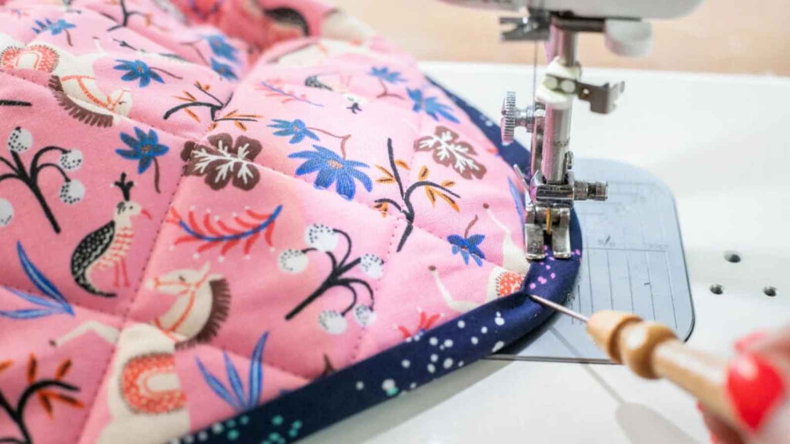 dark blue binding being sewn onto pink and blue quilted fabric.