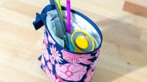 A bird's eye view looking down into a height-adjustable pencil/tool pouch on a well lit wooden desk filled with a pencil, rotary cutter, and scissors.