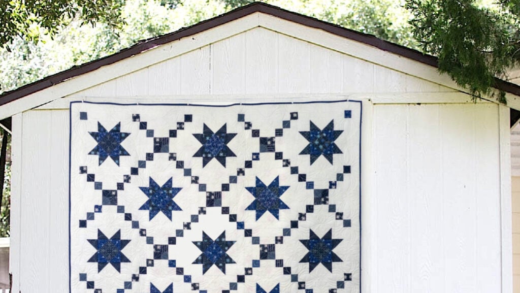 Blue and White quilt with stars and Irish Chain hanging on the side of a white barn.