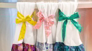 An easy sewing project showing three dish towels with colorful bows and ruffles sewn onto them.