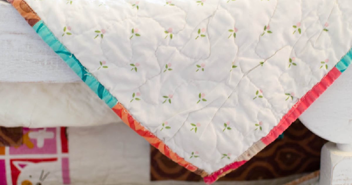 A large, vintage 100% cotton flat sheet with a delicate pastel floral pattern being used as a seamless quilt backing. This clever thrift store sewing hack provides several yards of high-quality, pre-shrunk fabric, perfect for creating an affordable and sustainable heirloom quilt.
